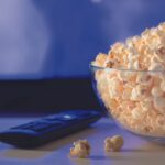 Popcorn in a Glass Bowl and a TV rEMOTE onn Top of a Table